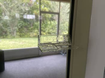 reviewer photo of the clear plastic Burglabar attached to a window pane with the latch flipped up