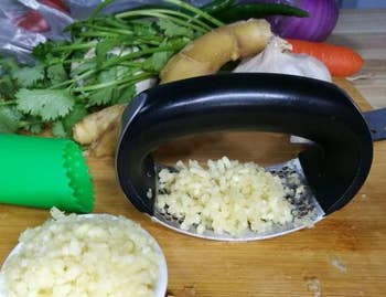 Garlic crushed in a press, with vegetables and a garlic roller in the background. Useful for cooking tasks