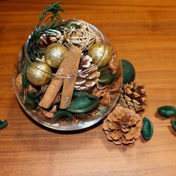 mix of pine needles, citrus, pine cones, and decorative pieces in a glass bowl