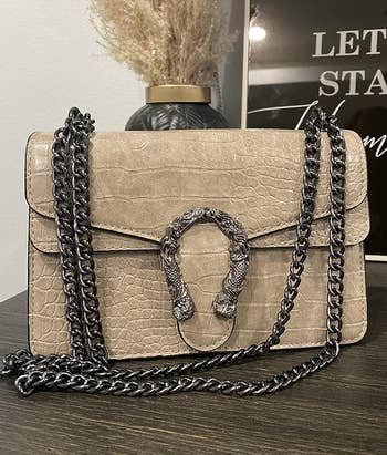Tan handbag with a metallic concatenation strap and a snakeskin accent