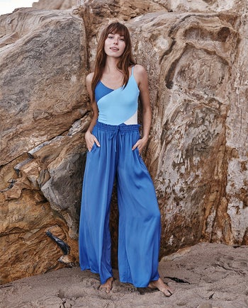 model standing near rock formation, wearing blue palazzo pants over blue colorblock one-piece swimsuit