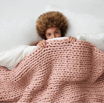 A model peeking out from under a pale pink thickly woven blanket 