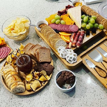 reviewer photo of the square charcuterie board and round snack tray filled with meats, crackers, cheese, and fruit
