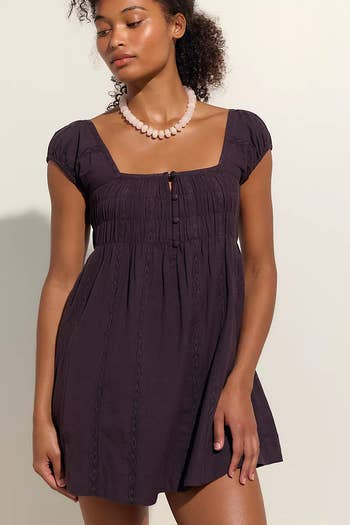 Model wearing a stylish short-sleeve, square-neck dress with a bead necklace, posing for a shopping article