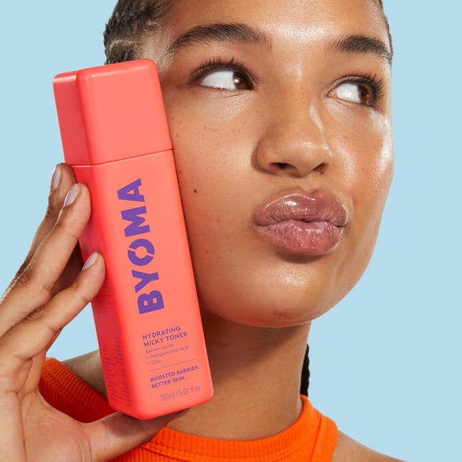 Person holding a vessel of BYOMA Hydrating Milky Toner adjacent their face, appearing thoughtful