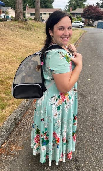 reviewer in a floral dress smiles, carrying a pet carrier with a visible dog inside