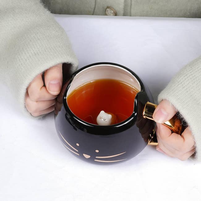 Hands holding a novelty cat-shaped mug with tea