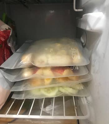 reviewer's freezer containing four of the reusable bags holding various produce and neatly stacked