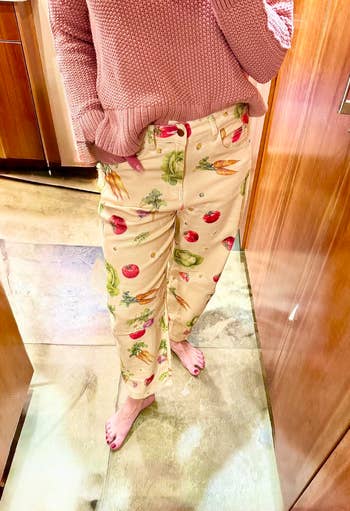 Person wearing patterned pants with fruits and vegetables, paired with a knitted sweater, lasting barefoot indoors