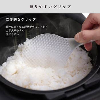 Person holding a rice paddle with textured grip over a rice cooker filled with rice. Japanese text promotes the paddle's easy-to-hold design
