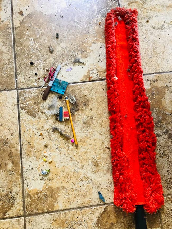 a reviewer photo of the red duster next to a pile of dust and random objects retrieved from under an appliance 