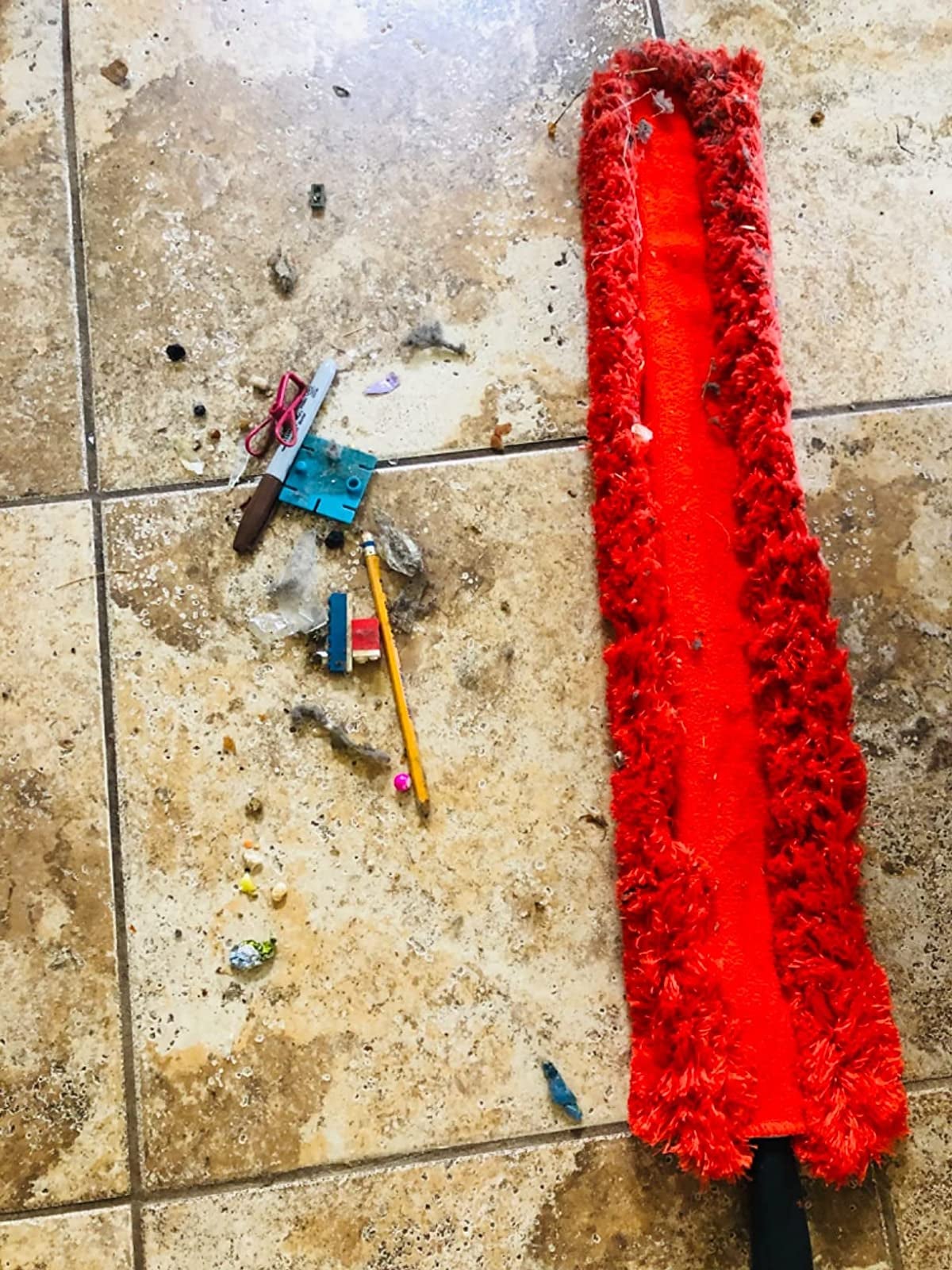a reviewer photo of the red duster next to a pile of dust and random objects retrieved from under an appliance 