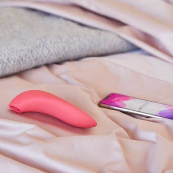 Pink suction vibrator on bed next to cell phone
