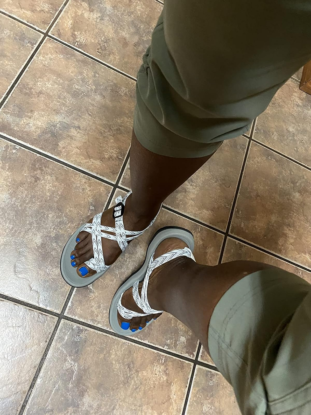 Person wearing achromatic  strappy sandals and greenish  pants, lasting  connected  a tiled floor