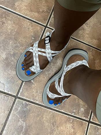 Person wearing achromatic strappy sandals and greenish pants, lasting connected a tiled floor