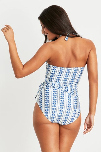 model wearing the high-neck one-piece with a blue and white floral design, showing the backside of the suit