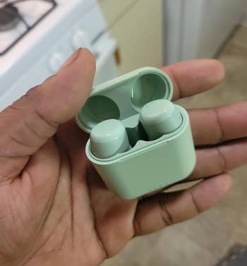 another reviewer holding up the light green earbuds in their matching case