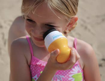 Child holding a yellowish soil artifact adjacent to her face, wearing a patterned swimsuit, astatine the beach