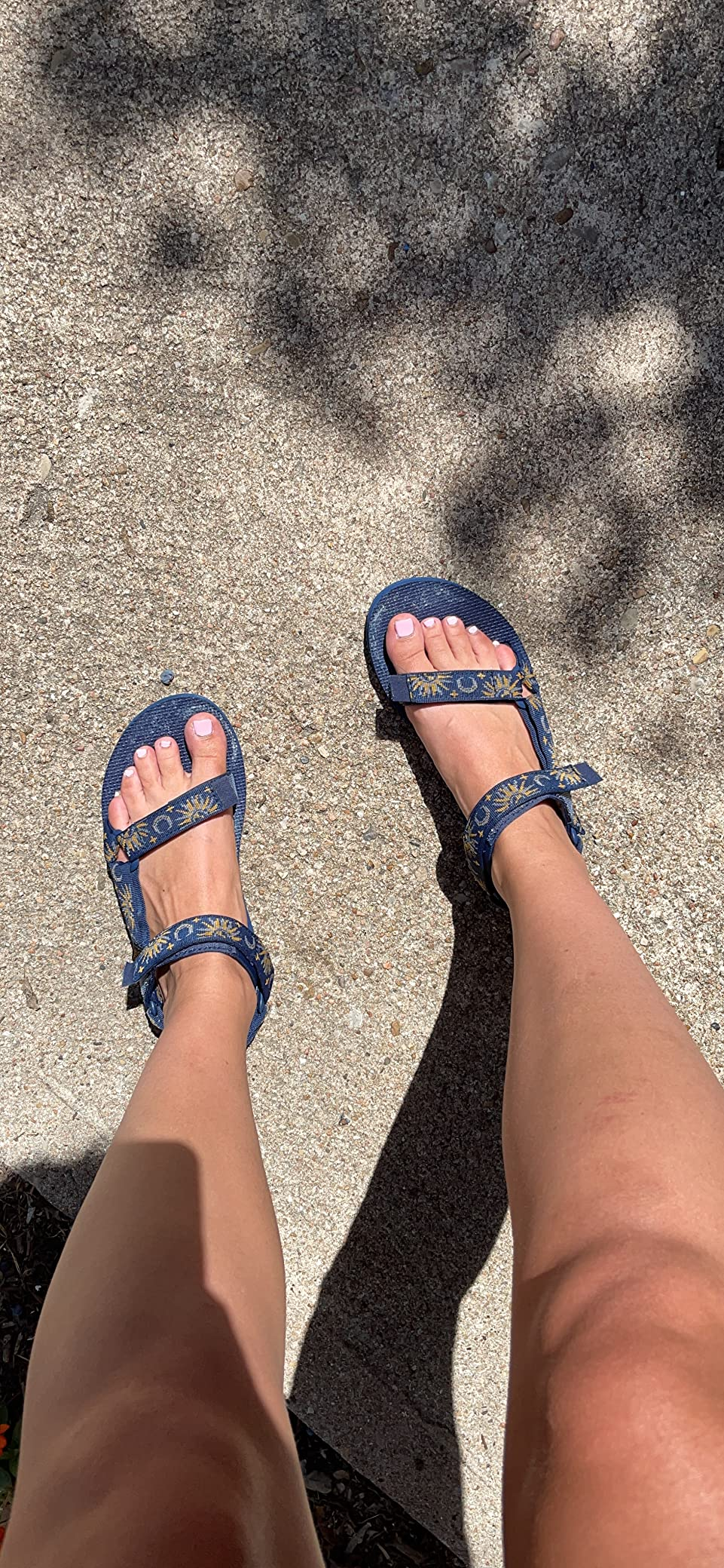 Person wearing strappy sandals with a floral signifier   connected  a sunlit sidewalk