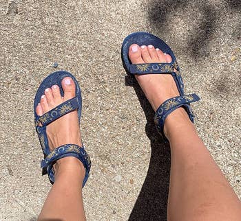 Person wearing strappy sandals with a floral signifier connected a sunlit sidewalk