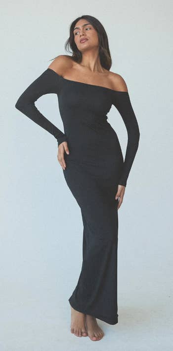 model in a black off-shoulder dress with long sleeves, standing barefoot