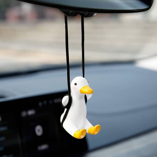 A white duck figure suspended on a black swing from a car mirror 
