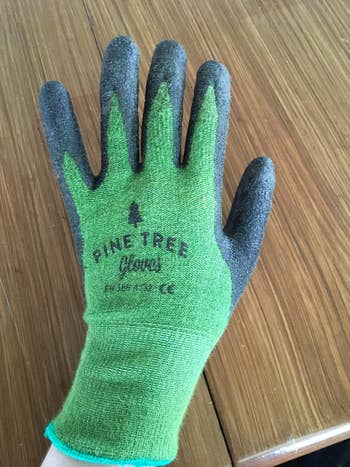 A hand wearing a green and black gardening glove labeled 