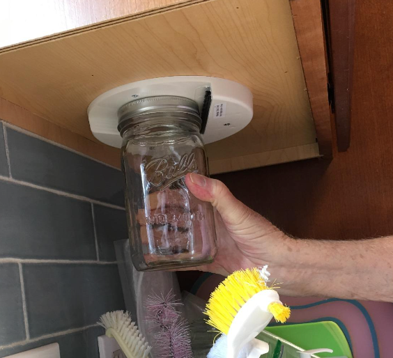 reviewer's hand opening a jar with the attachment under their cabinet 