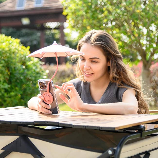 A model using a phone with a mini umbrella attachment at an outdoor table