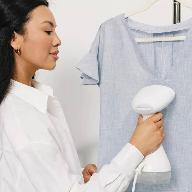 Person utilizing a handheld garment steamer connected  a garment  hanging connected  a rack