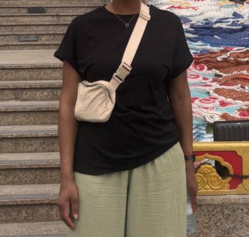 Person wearing a achromatic  t-shirt, beige crossbody bag, and airy  pants, lasting  connected  steps with an ornate background