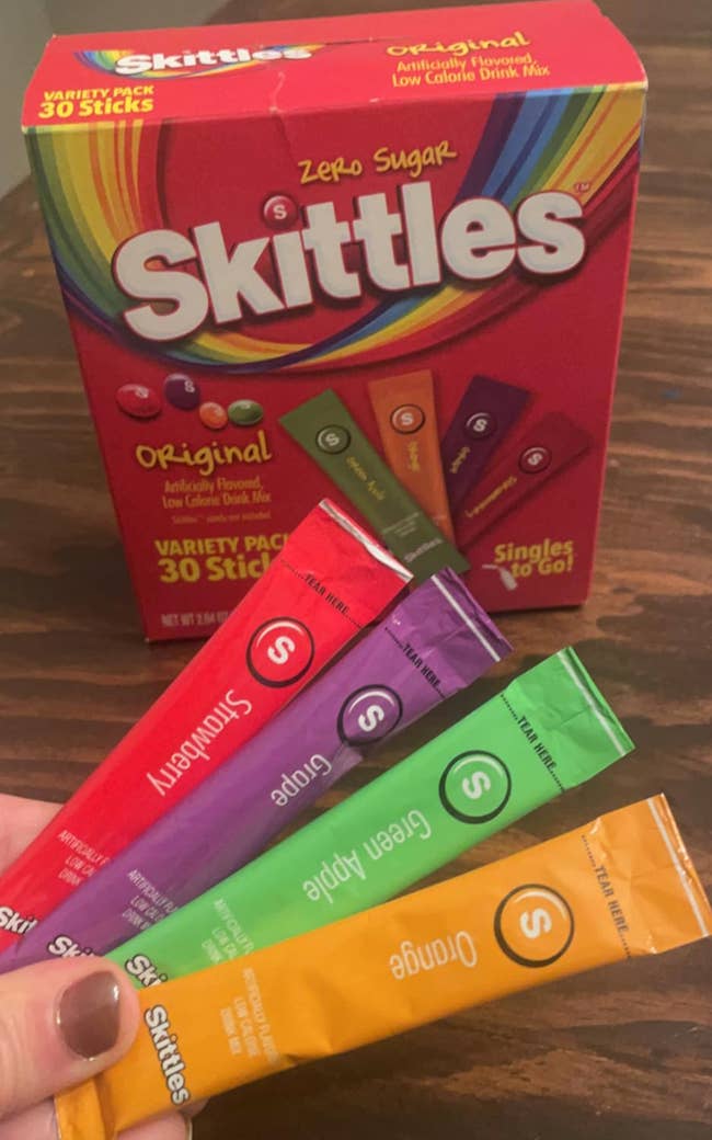 Hand holding Skittles Sugar Free drink mix packets in front of the product box
