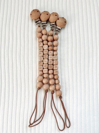 four wooden pacifier clips with different names on them