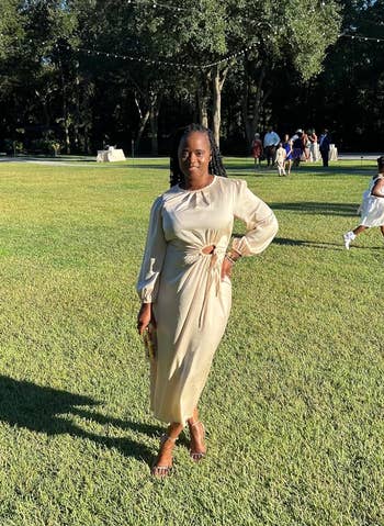 Reviewer in elegant beige dress posing on grass with attendees in background. Perfect for a chic outdoor event