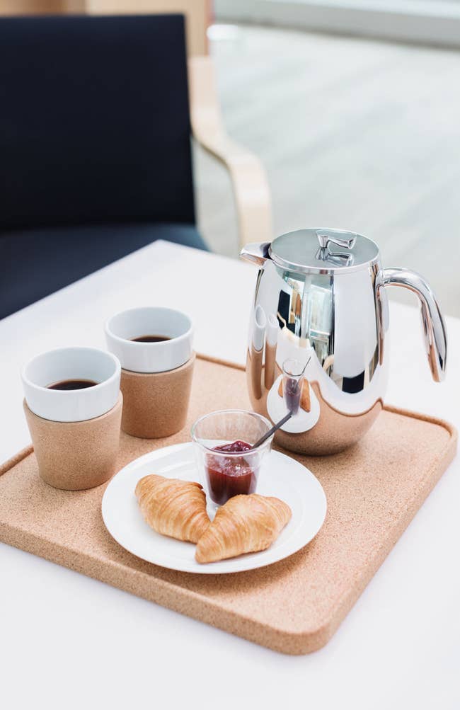 Tray with java pot, 2 cups, croissants, and jam connected a table, suggesting a cozy meal setting