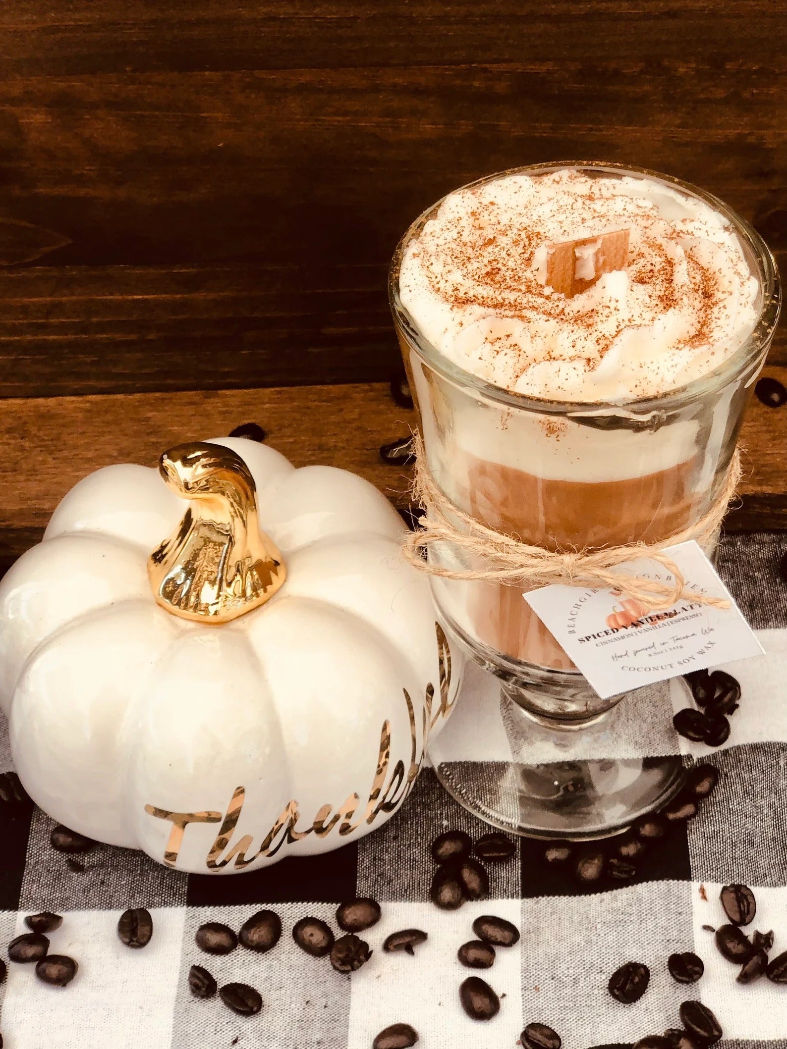 a candle that looks like a coffee latte in a glass mug next to a white pumpkin that reads