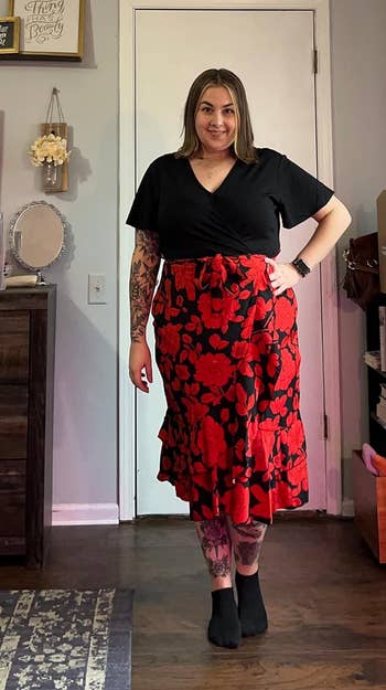 A person wearing a black top and red floral skirt posing with hands on hips