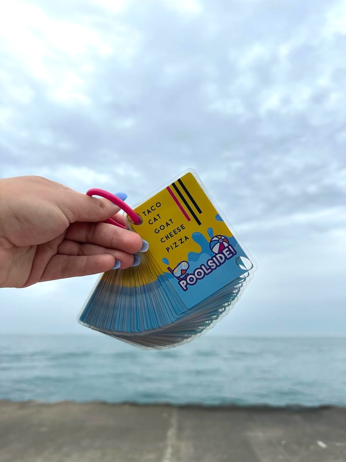 A manus  holds a acceptable   of Poolside! paper  crippled  cards with Taco Cat Goat Cheese Pizza substance   connected  the apical  card, adjacent   a formation  backdrop
