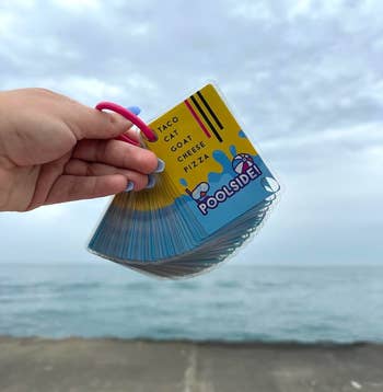 A manus holds a acceptable of Poolside! paper crippled cards with Taco Cat Goat Cheese Pizza substance connected the apical card, adjacent a formation backdrop