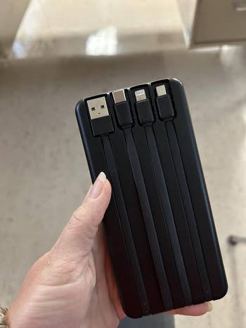 Hand holding a achromatic multi-device charging presumption with integrated cables for USB, micro USB, Lightning, and USB-C connectors