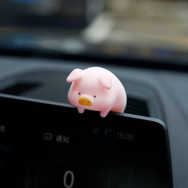 a small pink pig hanging over the lip of a car monitor