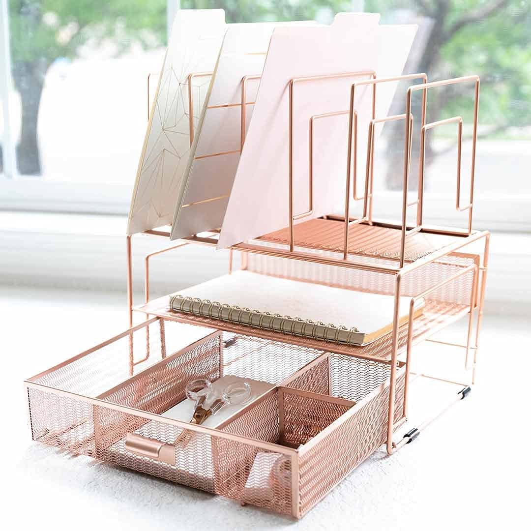Rose gold metal office organizer that holds folders, a notebook, and an open bottom drawer with other office supplies