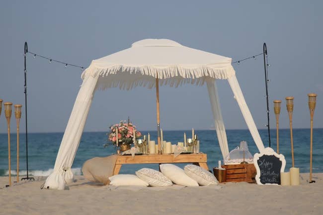 a reviewer's white canopy with tassels set up on a beach with a picnic under it
