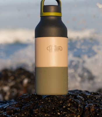 Reusable water bottle with dual-tone design and brand logo, placed on a rocky surface