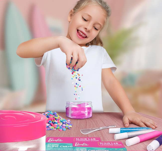 Child pouring colorful sprinkles into a jar, surrounded by crafting tools and materials connected a table