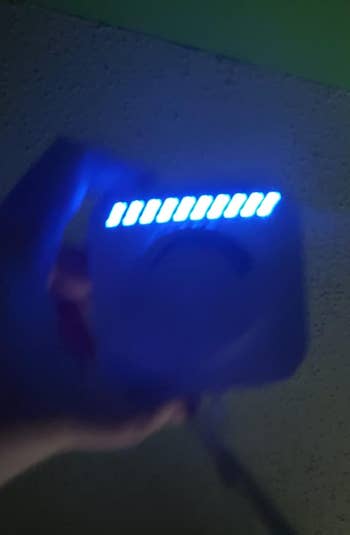 Hand holding a device with illuminated blue LEDs, possibly indicating power level or charge status