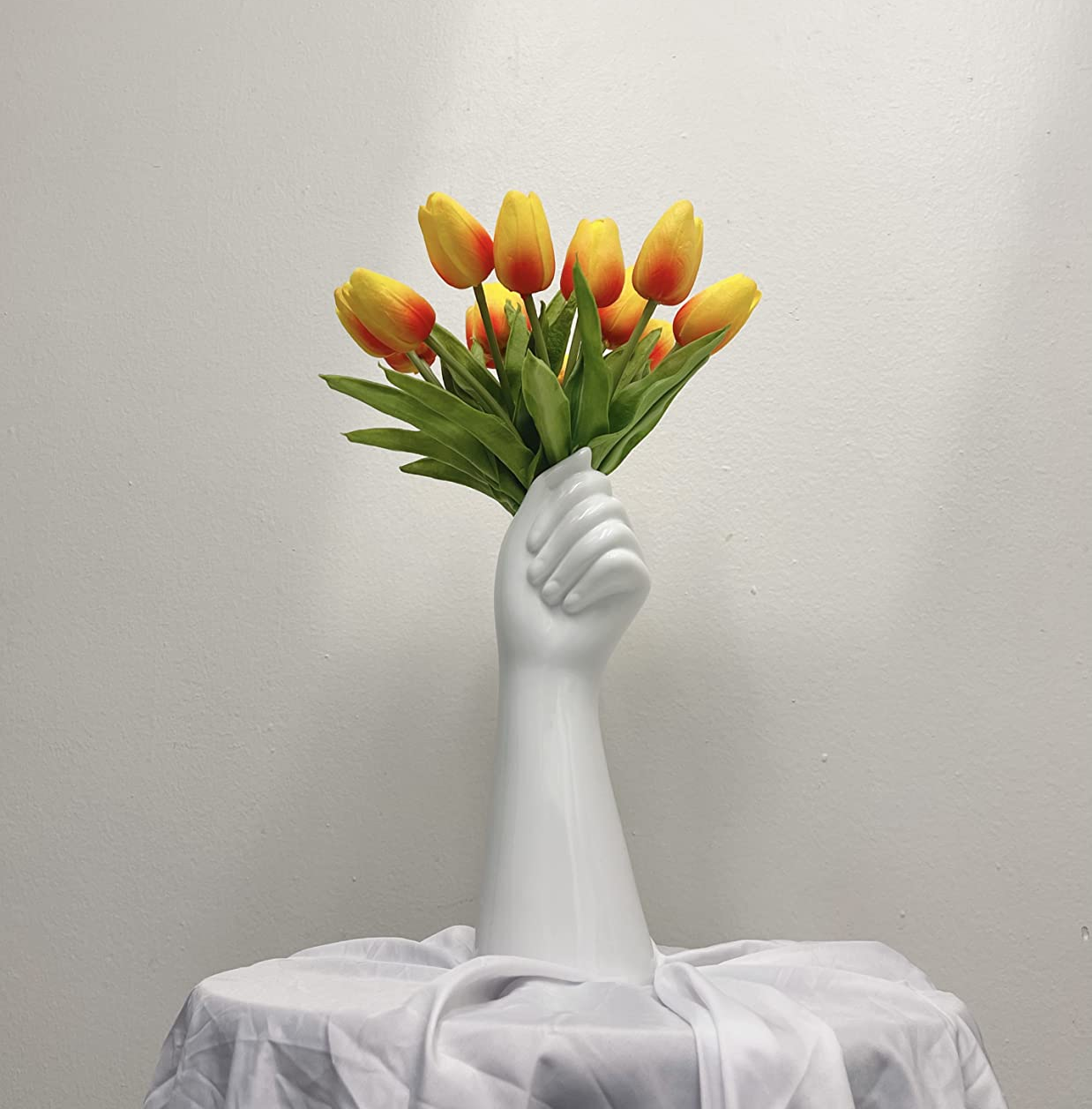 Reviewer image of yellow tulips inside a white hand-shaped vase on top of a table with a white tablecloth
