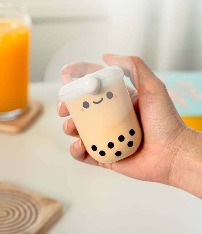 hand holding fan shaped like bubble tea cup with happy face