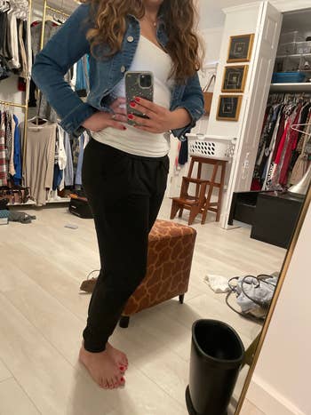 Person taking a reflector selfie successful a closet, wearing a denim jacket, achromatic top, and achromatic pants, with shelves and covering successful the background