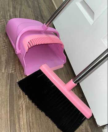 close up of a pink long handled dust bin with cleaning grooves with a pink broom 